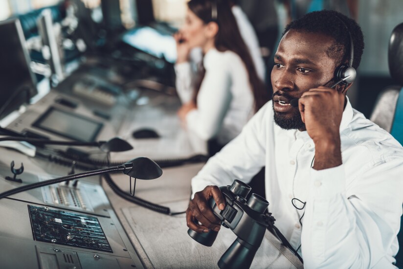 Center of dispatching maintenance. Waist up portrait of afro-american specialist speaking on headset microphone while working on navigation controller board