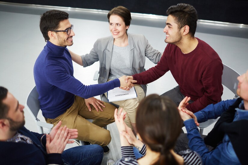 Happy men handshaking with helpful psychologist and applauding colleagues near by