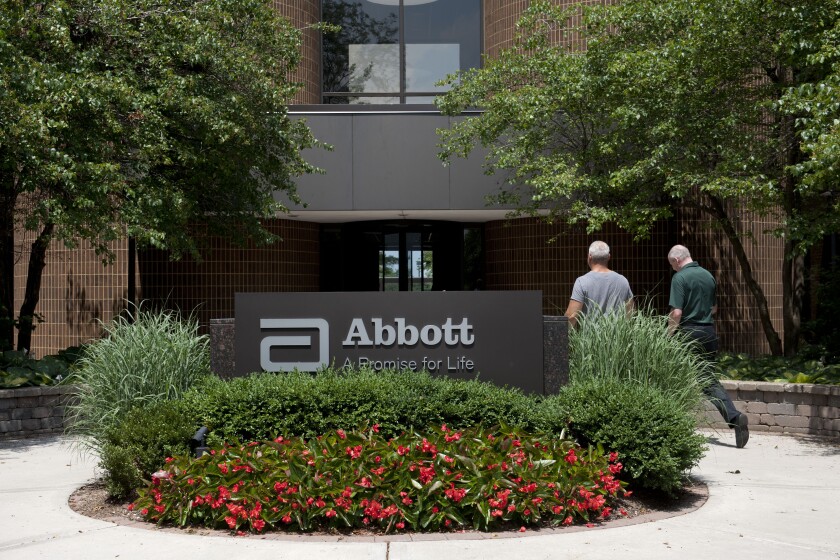 Employees walk near an Abbott Laboratories sign at the company's headquarters complex in Abbott Park, Illinois, U.S., on Monday, July 14, 2014. Abbott Laboratories said it plans to sell its generic drug business for established markets to Mylan Inc., getting in return a share of the newly combined companies in a deal valued at about $5.3 billion. Photographer: Daniel Acker/Bloomberg