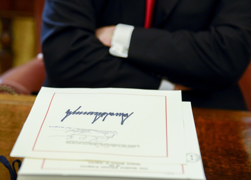 U.S. President Donald Trump sits next to a tax-overhaul bill after singing it into law in the Oval Office of the White House in Washington, D.C., U.S., on Friday, Dec. 22, 2017. This week House Republicans passed the most extensive rewrite of the U.S. tax code in more than 30 years, hours after the Senate passed the legislation, handing Trump his first major legislative victory providing a permanent tax cut for corporations and shorter-term relief for individuals. Photographer: Mike Theiler/Pool via Bloomberg