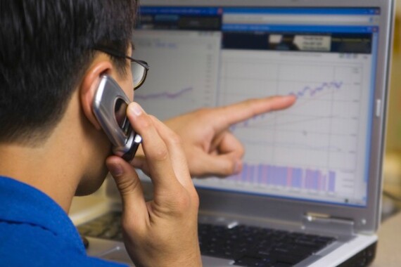 stock broker calling his client while looking at computer stock chart and pointing at the screen