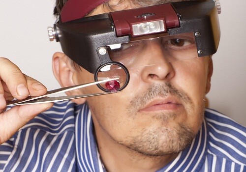 Male jeweler looking through a magnifier to check for flaws in a ruby. Focus on ruby