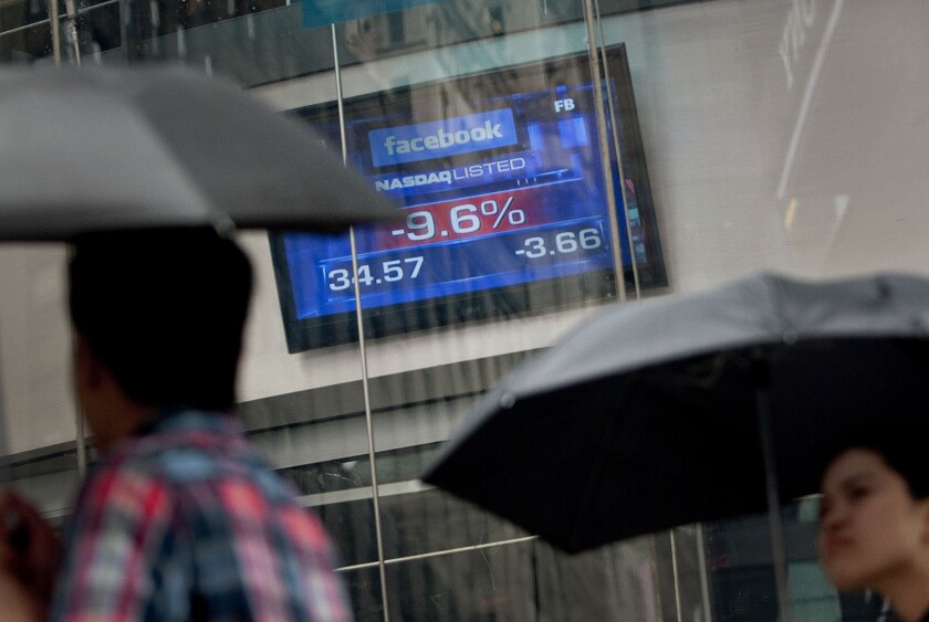Pedestrians walk past the share price for Facebook Inc. displayed at the Nasdaq MarketSite in New York.