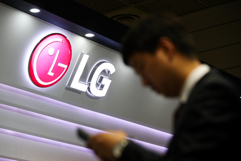 A visitor checks a smartphone in front of an LG Electronics Inc. logo displayed at the World IT Show 2018 in Seoul, South Korea/